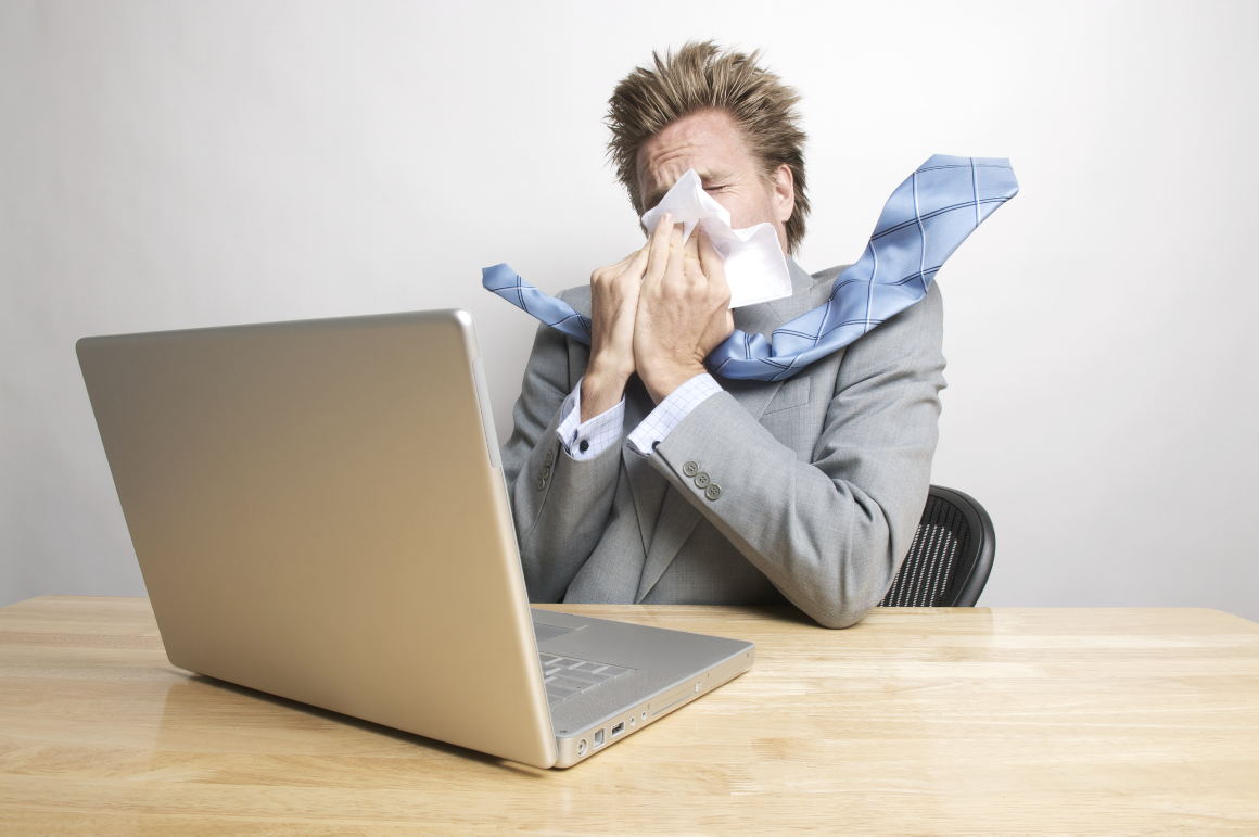 Man Sneezing at Desk in Front of Laptop